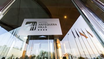 Senyal per HOTEL ANTEQUERA HILLS, amb façana de vidre moderna i banderes visibles al fons.