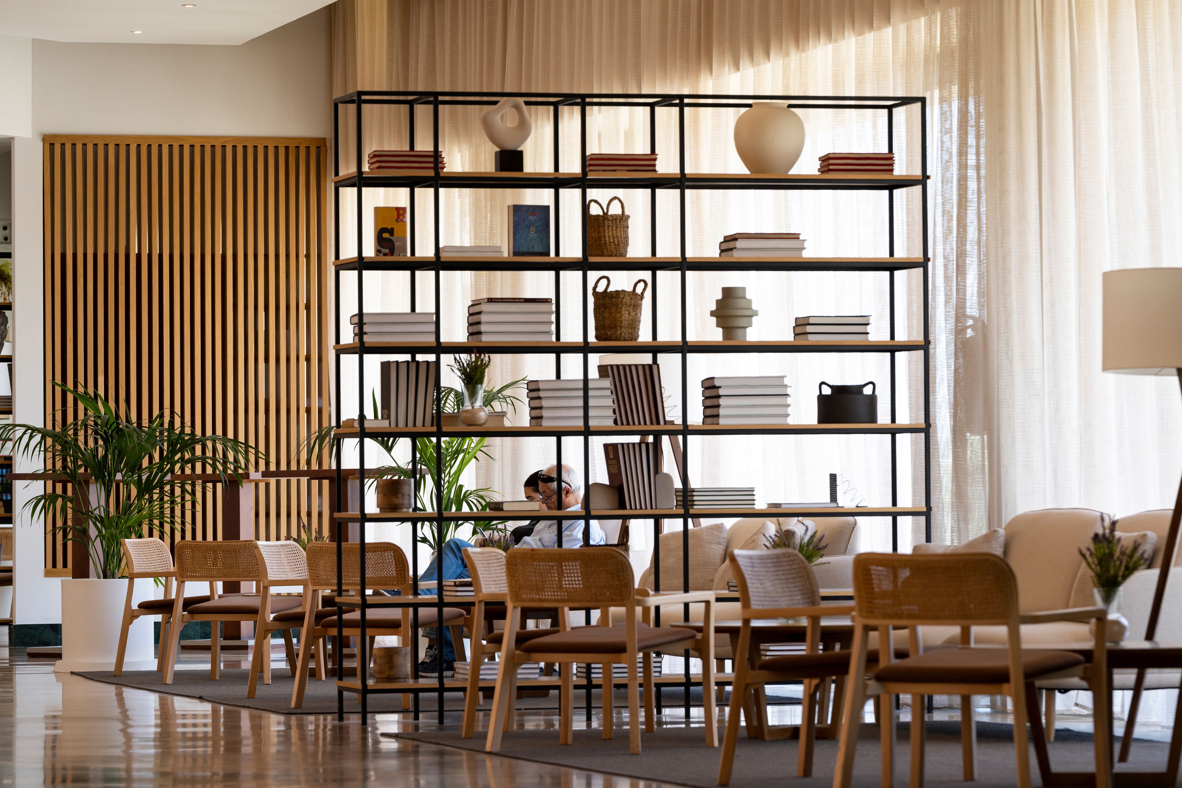 Uma sala de estar moderna com uma grande estante, assentos confortáveis e uma janela ampla com cortinas leves.