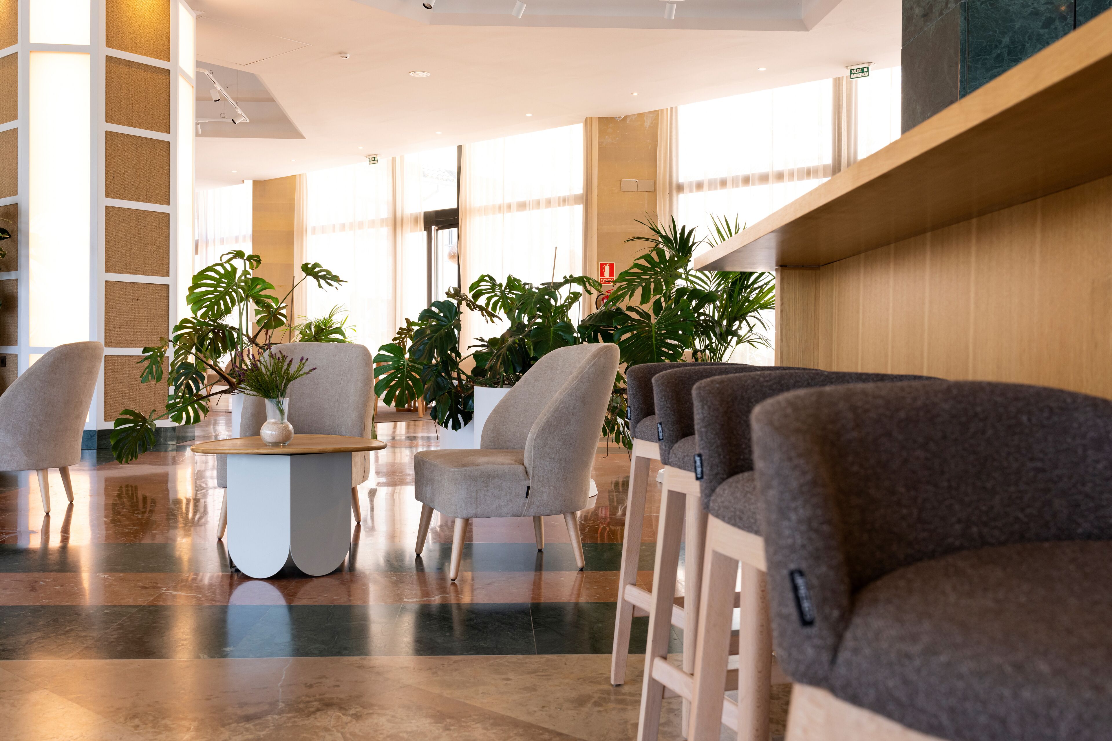 Un lobby moderno con asientos, plantas y un suelo pulido.