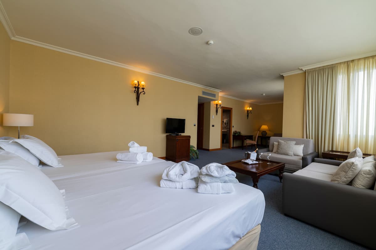 A hotel room with two beds, a sofa, a coffee table, and a TV.