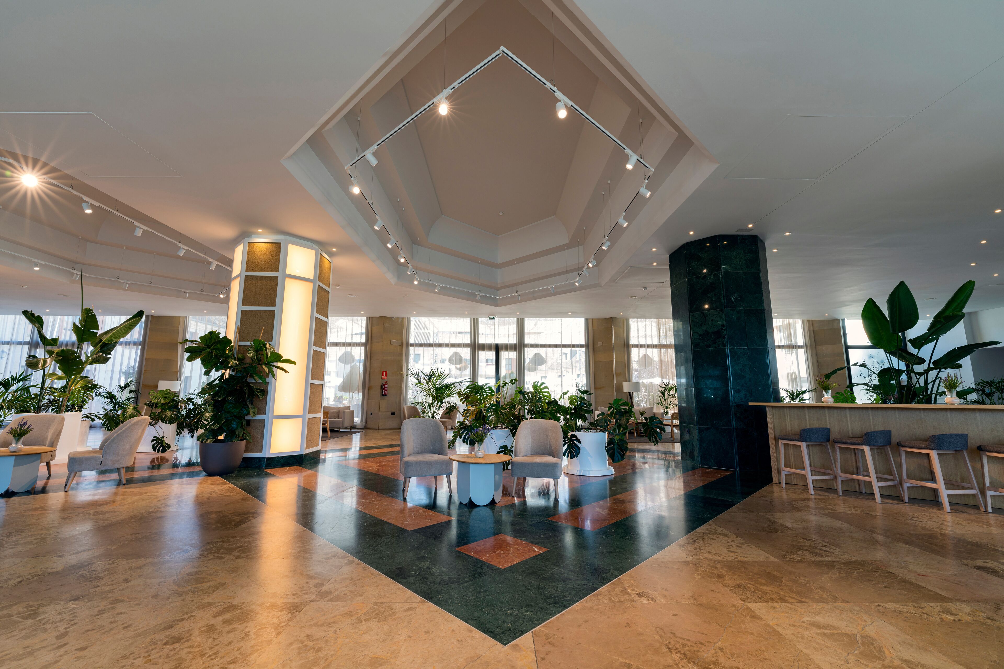 A spacious lobby with a high ceiling, multiple seating areas, and large windows allowing natural light.