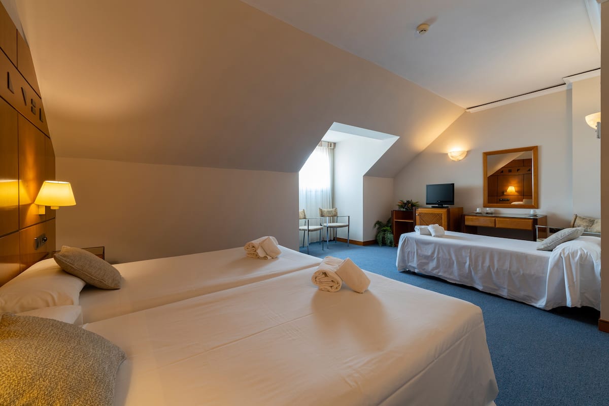 A hotel room with two beds, a desk, a chair, and a TV.