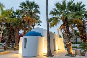 A modern building with a dome, surrounded by palm trees and a clear sky.