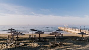 A beach with sun loungers and umbrellas, a walkway along the shore, and a clear view of the ocean. - Elias Beach Hotel (Limassol)
