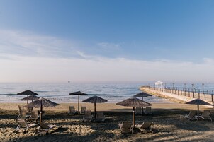 Di pantai, pasir putih, kursi berjemur, dan payung pantai