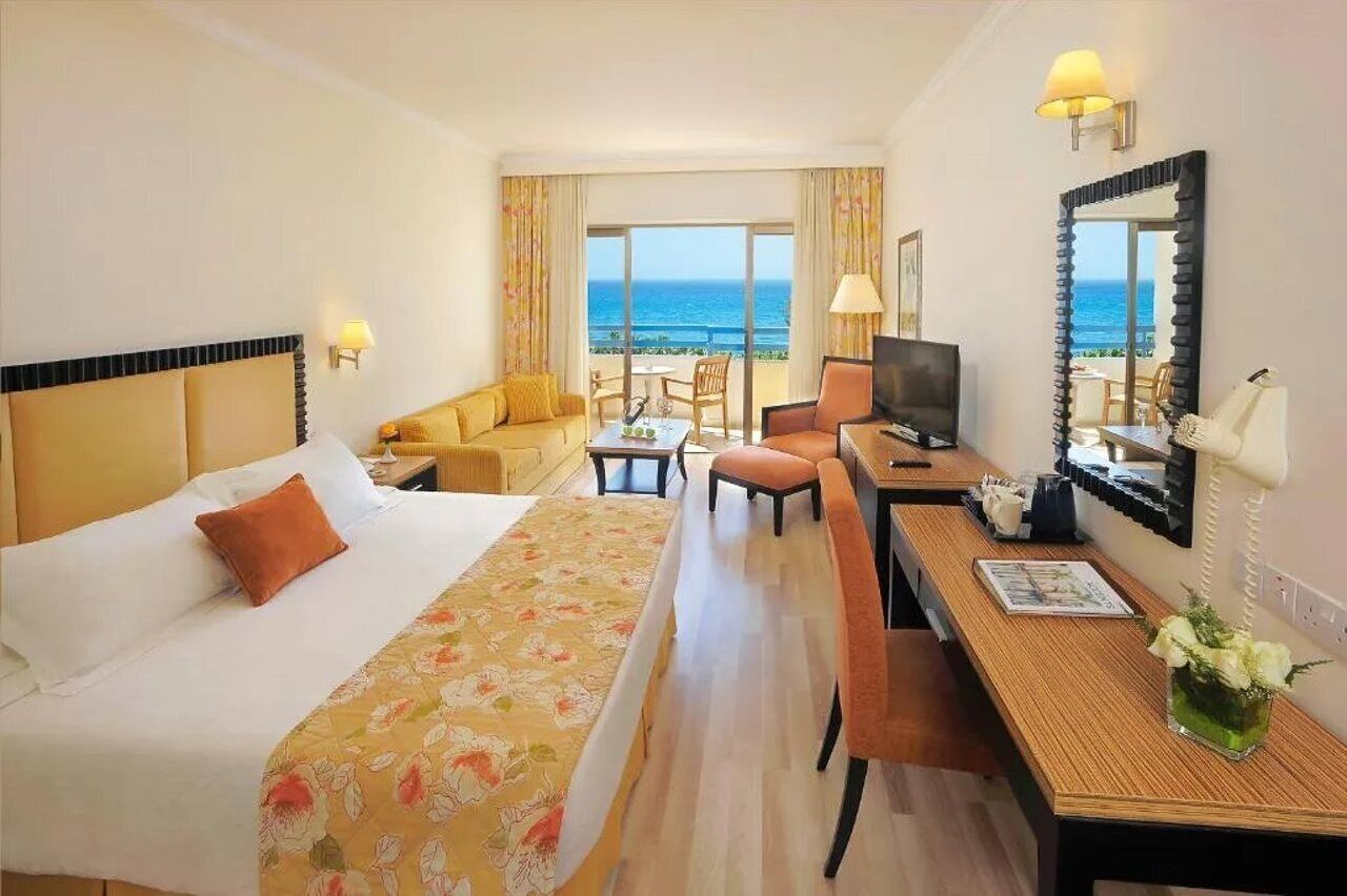 A hotel room with a bed, a desk, a TV, and a view of the ocean.