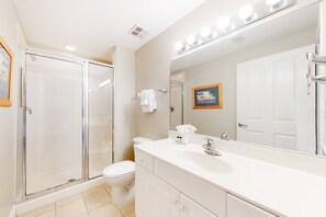 A modern bathroom with a glass shower enclosure, a white sink, and a large mirror with lights. - Celadon Beach Resort (Panama City Beach)