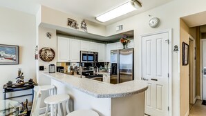 Una cucina moderna con mobili bianchi, elettrodomestici in acciaio inossidabile e un'area bar con sgabelli.