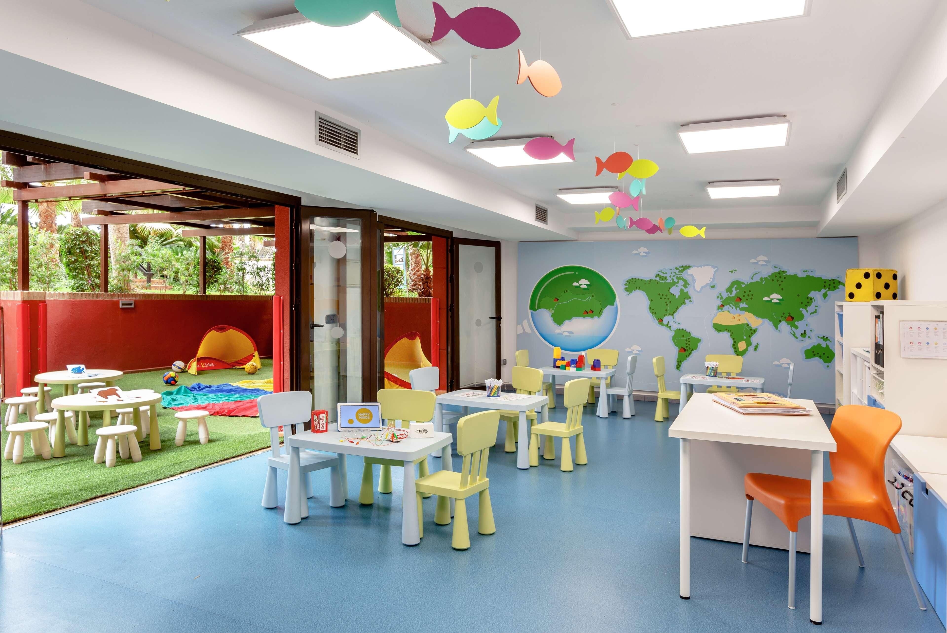 Une salle de jeux pour enfants avec des tables, des chaises et un mur décoré d’une carte du monde.