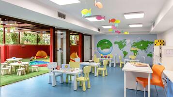 Une salle de jeux pour enfants avec des tables, des chaises et un mur décoré d’une carte du monde.