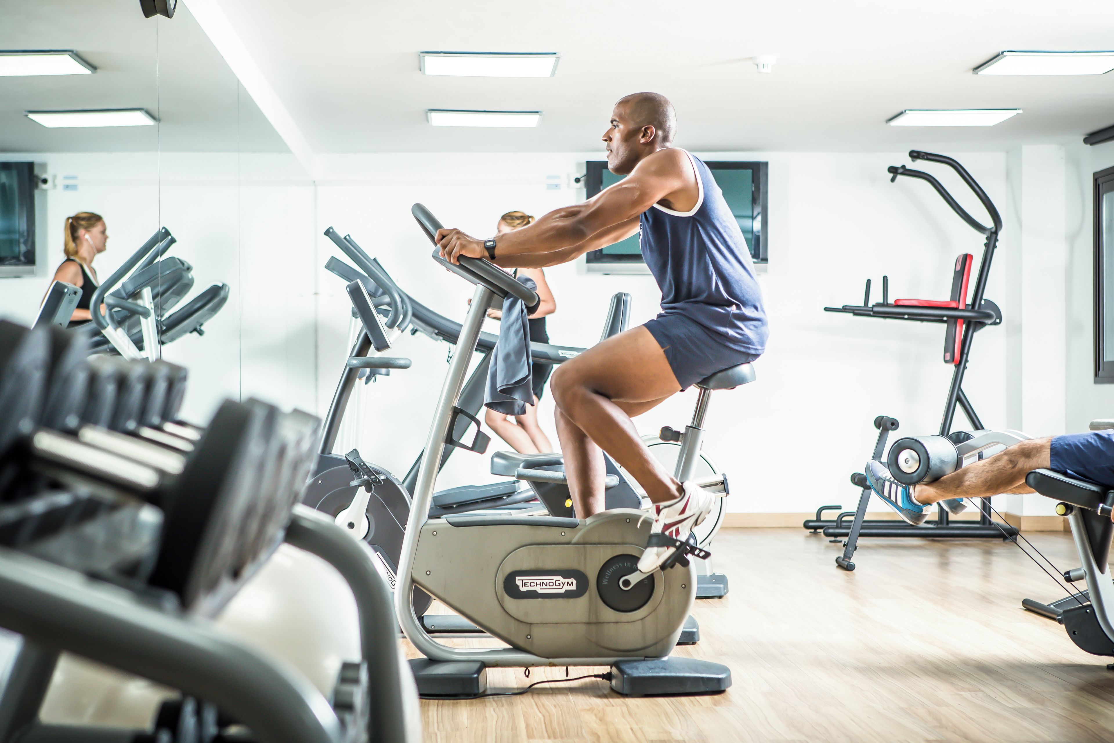 A gym with exercise equipment, mirrors, and a wooden floor.