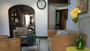 A living room with two sofas, a coffee table, and a small round table with a vase. There is a clock on the wall and a door with a 'no smoking' sign. - The Budget Hotel (Hazerswoude-Rijndijk)