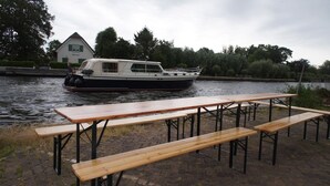 A riverside picnic area with wooden benches and a boat docked in the background. - The Budget Hotel (Hazerswoude-Rijndijk)