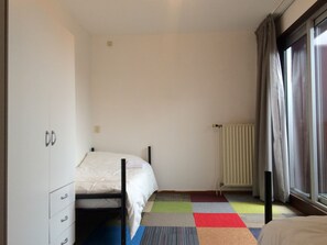 Ein Schlafzimmer mit Bett, Kleiderschrank, Heizkörper und einem Fenster mit Vorhängen.