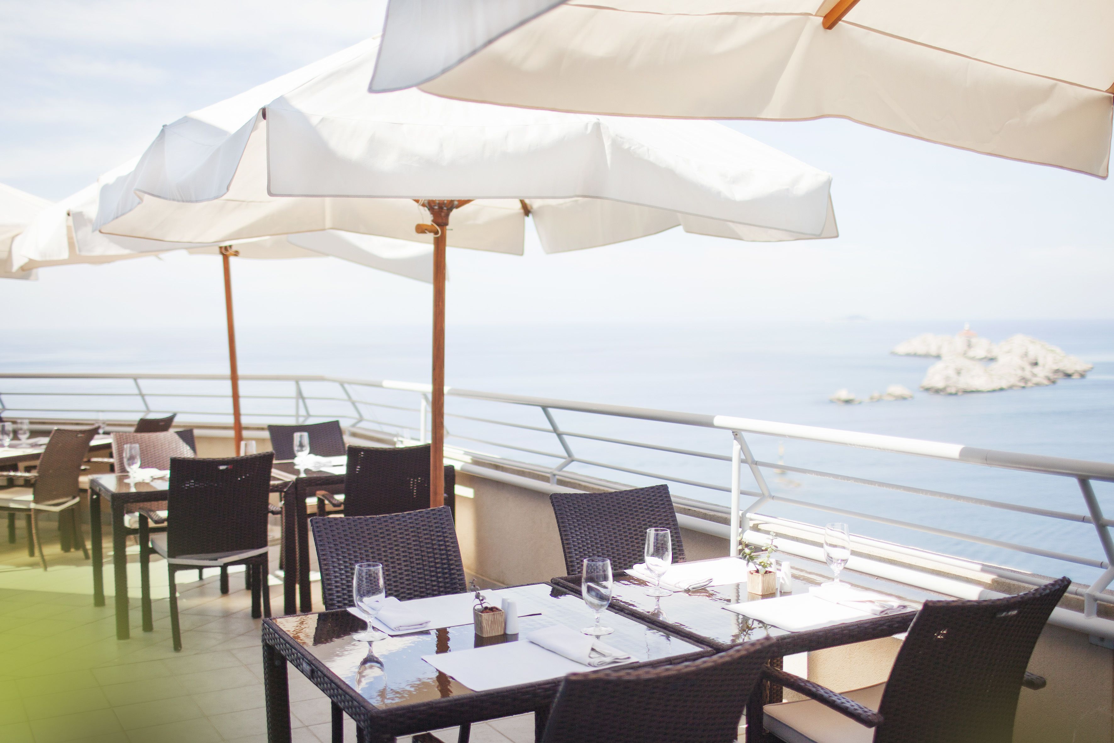 Un comedor con mesas y sillas, sombrillas blancas y vista al mar.