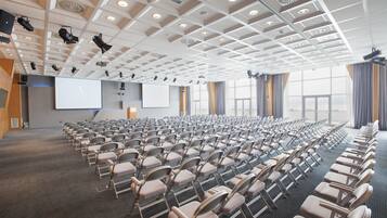 Une salle de conférence avec des rangées de chaises, un grand écran et un pupitre.