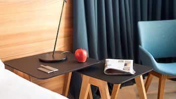 Une chambre d’hôtel avec un lit, une petite table avec une lampe, une pomme et un magazine.
