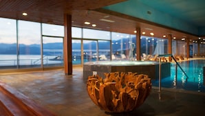 Un área de piscina interior moderna con un banco de madera y una gran pieza escultórica central.