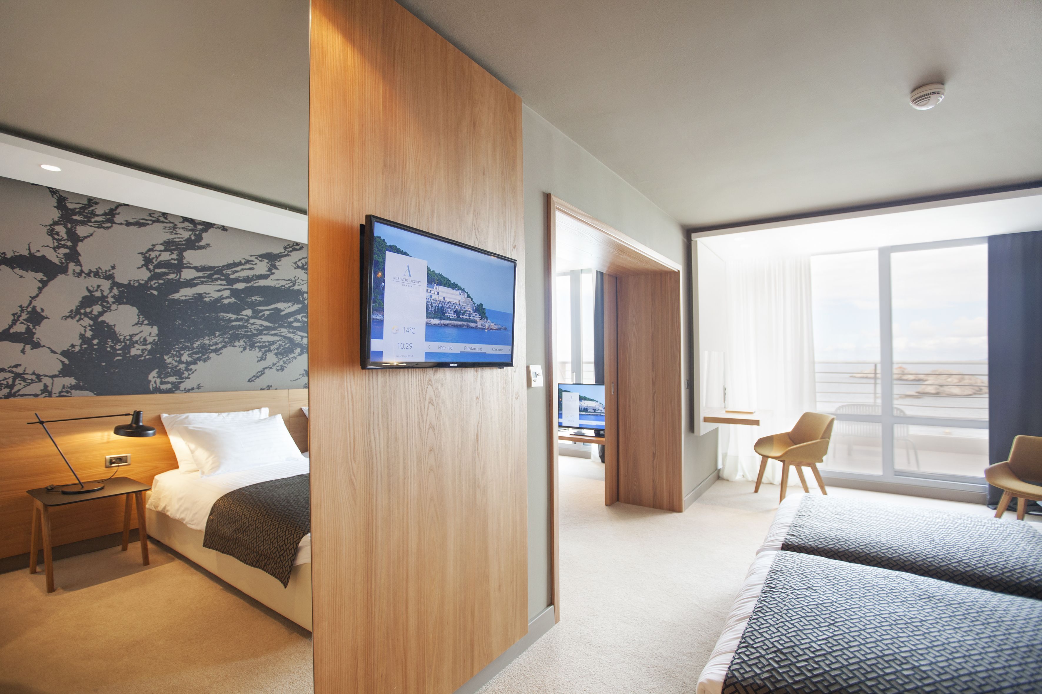 A modern hotel room with a bed, bedside table, TV, and a large window.