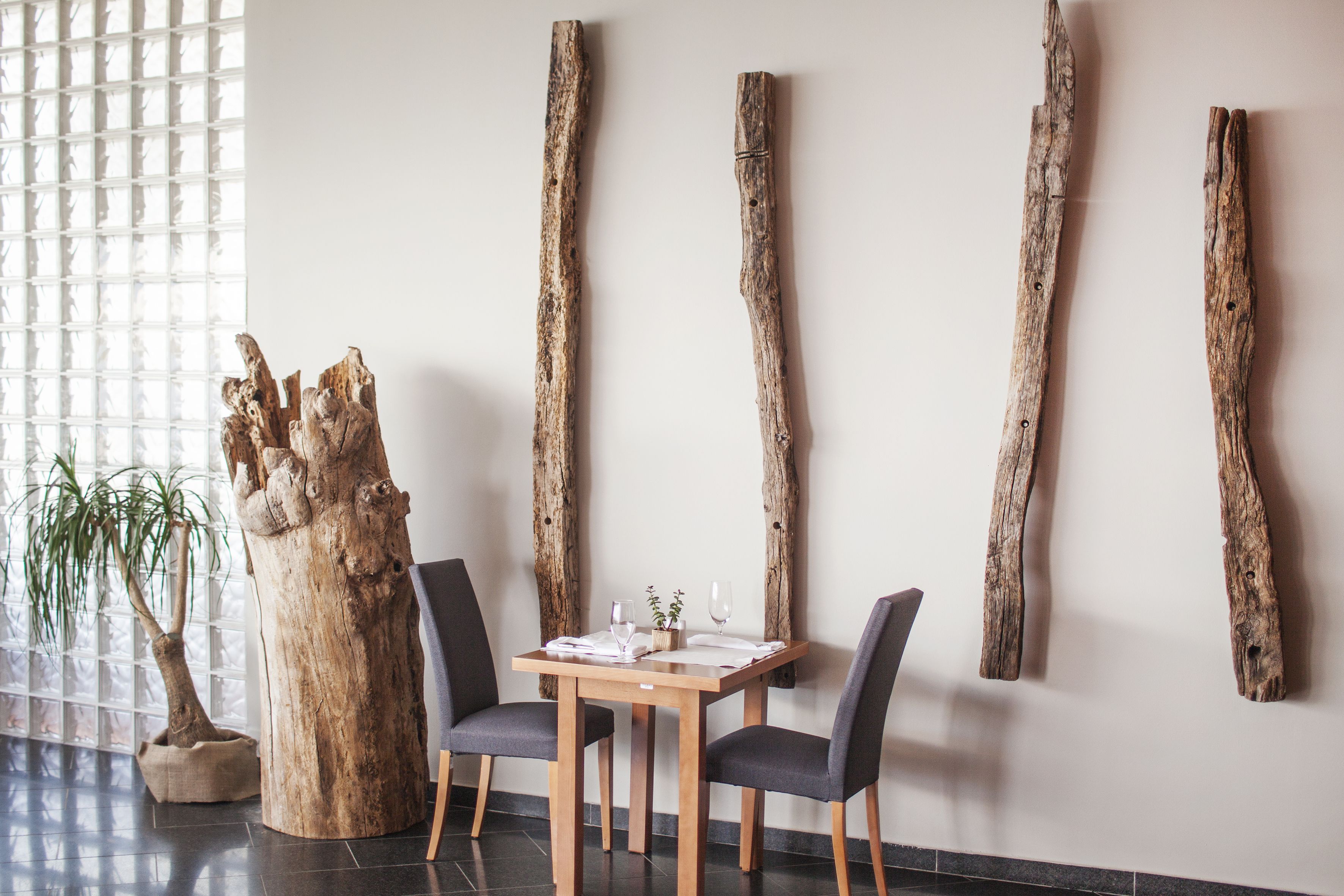 Uma área de refeições com uma mesa e cadeiras de madeira, uma escultura de tronco de árvore e um vaso com planta.