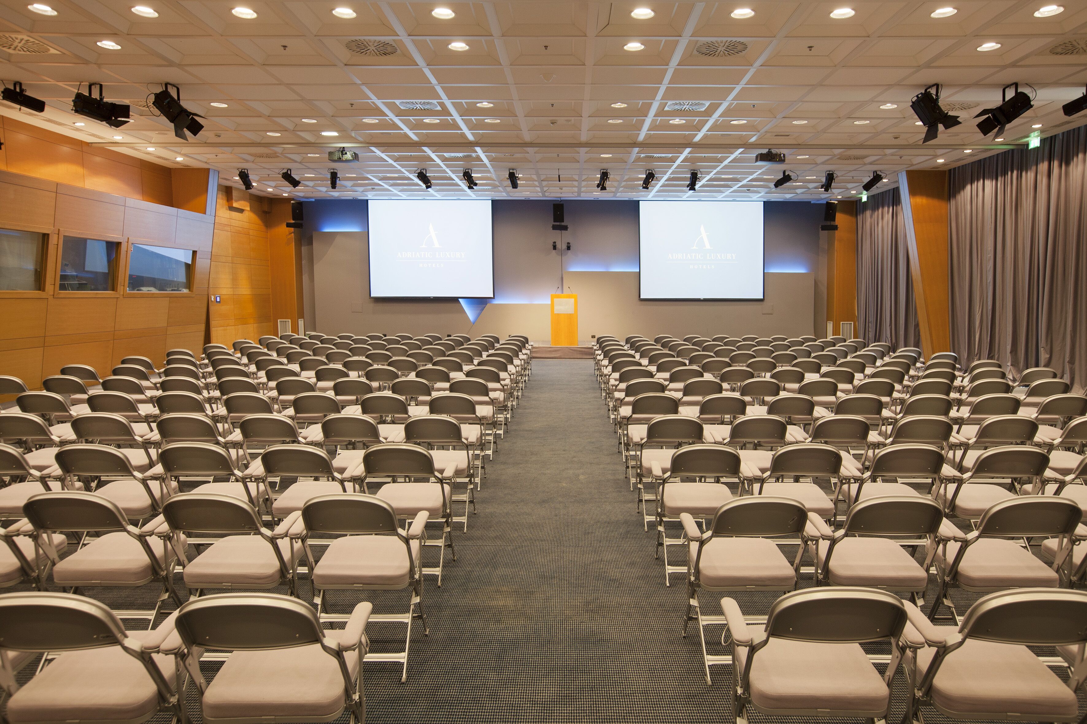 A conference room with rows of chairs, a large screen, and a podium.