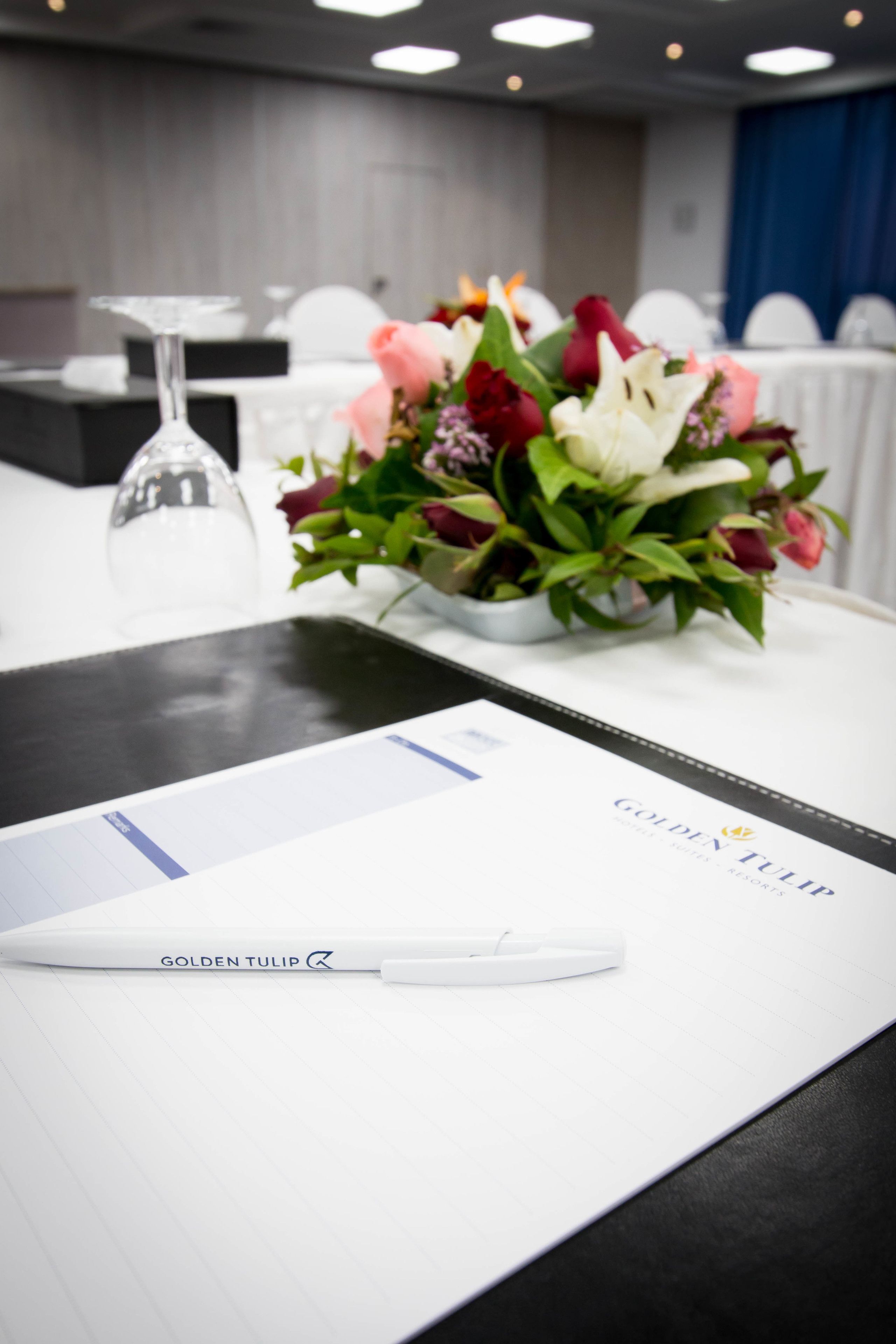 Una mesa con un bloc blanco, un bolígrafo y un ramo de flores.