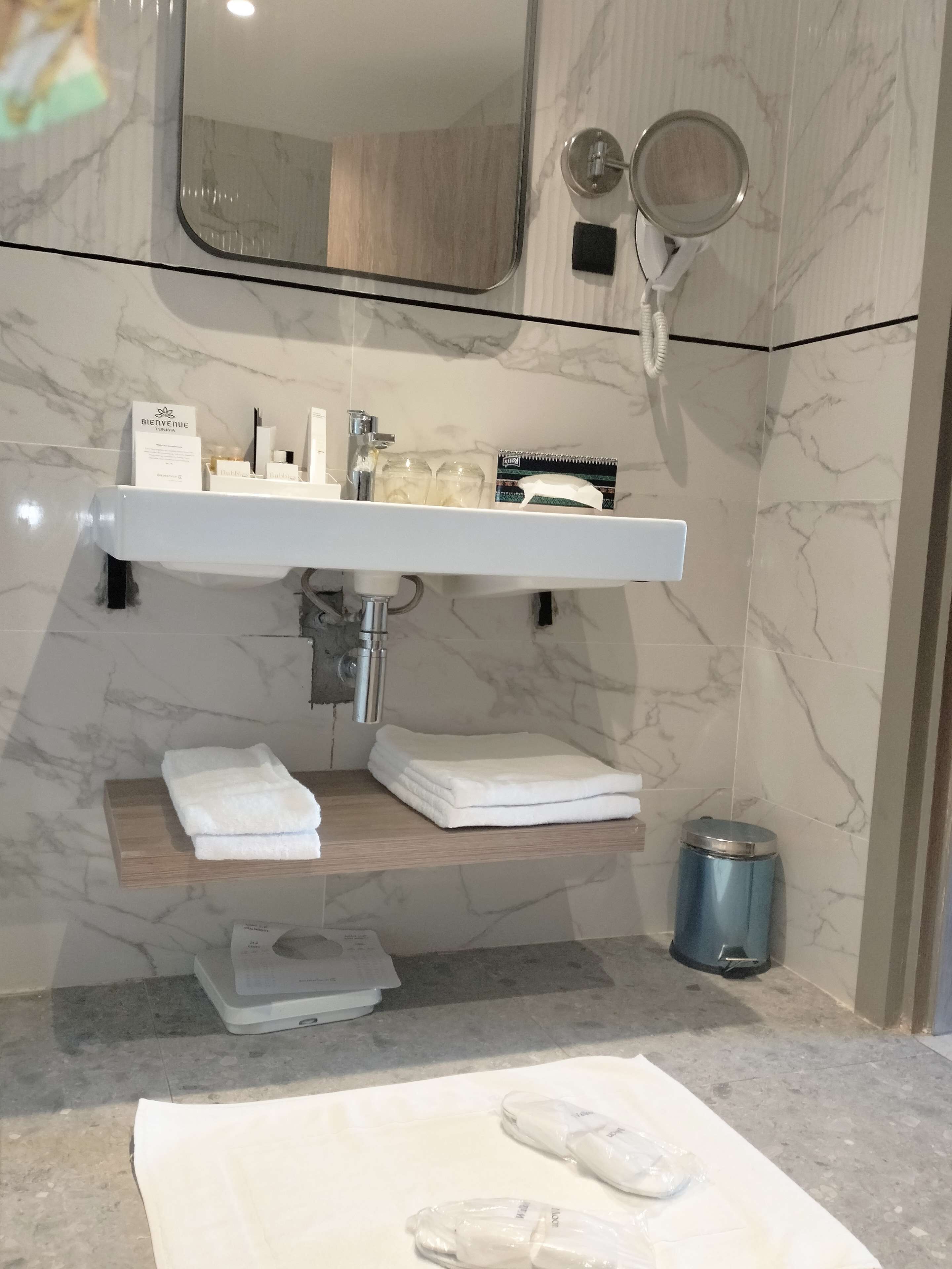 Un baño con pared de azulejos de mármol, un lavabo blanco, un espejo y un perchero para toallas.