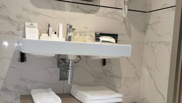 Un baño con pared de azulejos de mármol, un lavabo blanco, un espejo y un perchero para toallas.