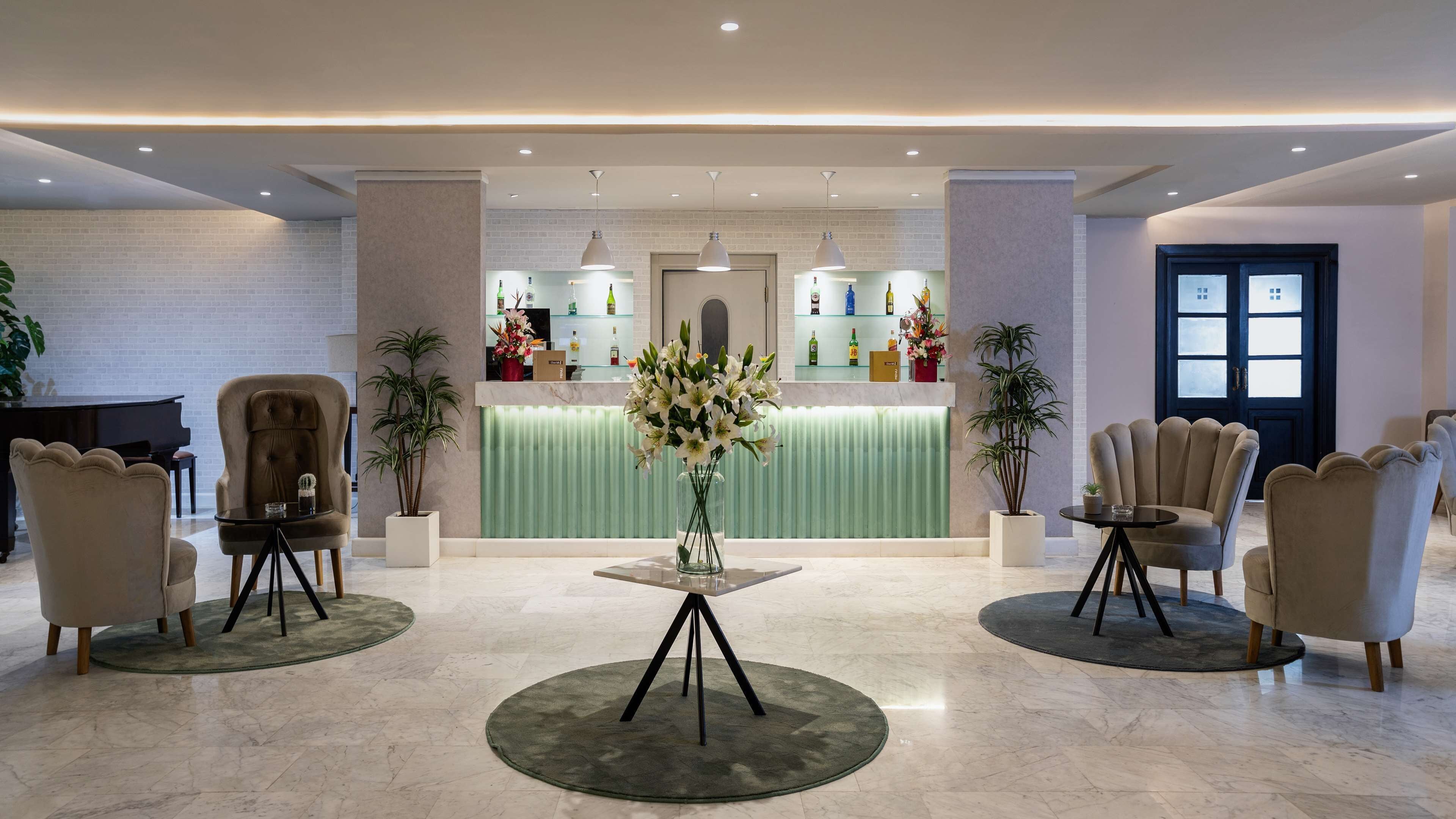 A lobby with a reception desk, two armchairs, a piano, and a vase of flowers.