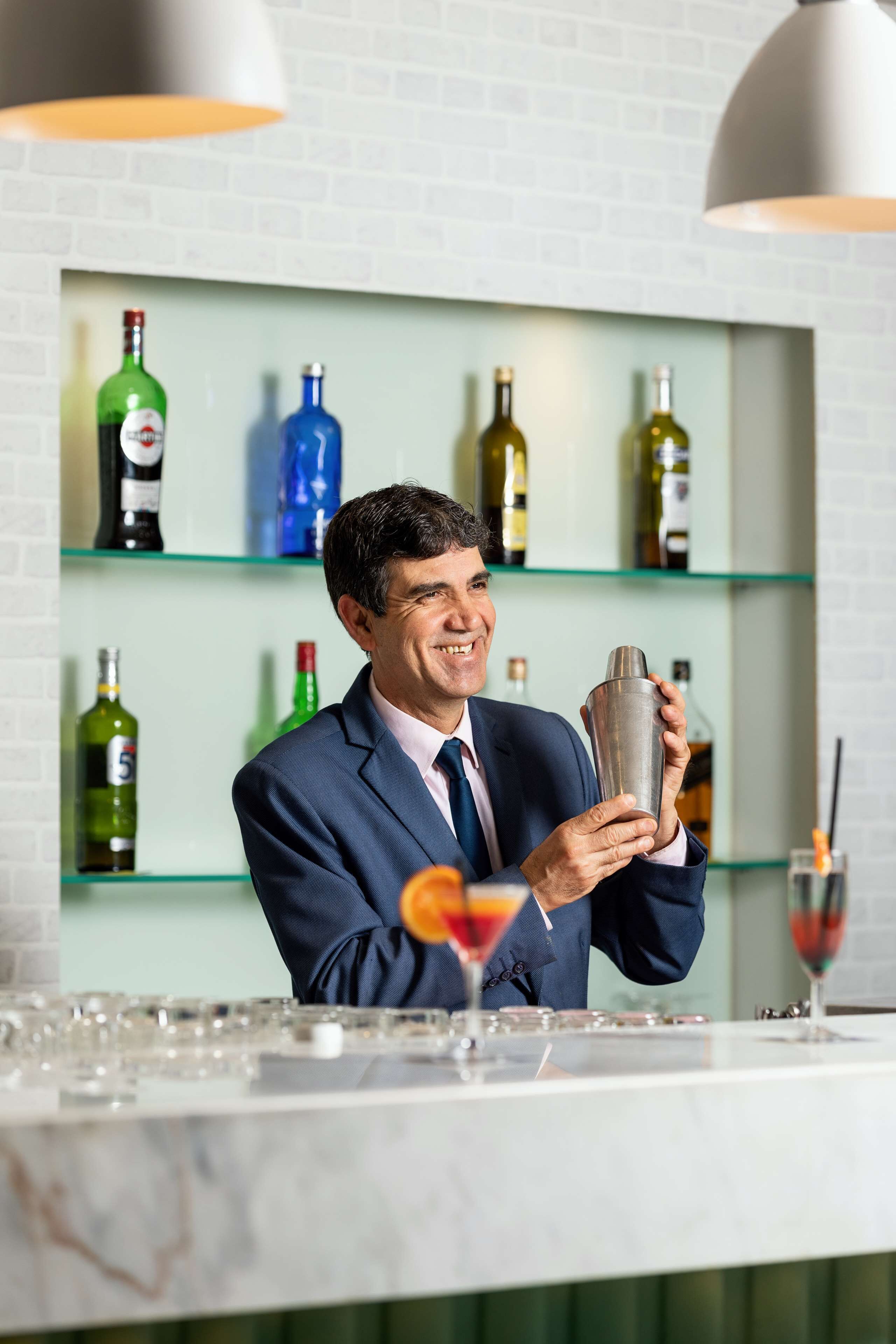 Un espace bar avec des étagères remplies de bouteilles d’alcool, un comptoir et un shaker à cocktails.