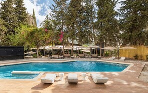 A swimming pool with lounge chairs and umbrellas, surrounded by trees and a building. - Golden Tulip El Mechtel (Tunis)
