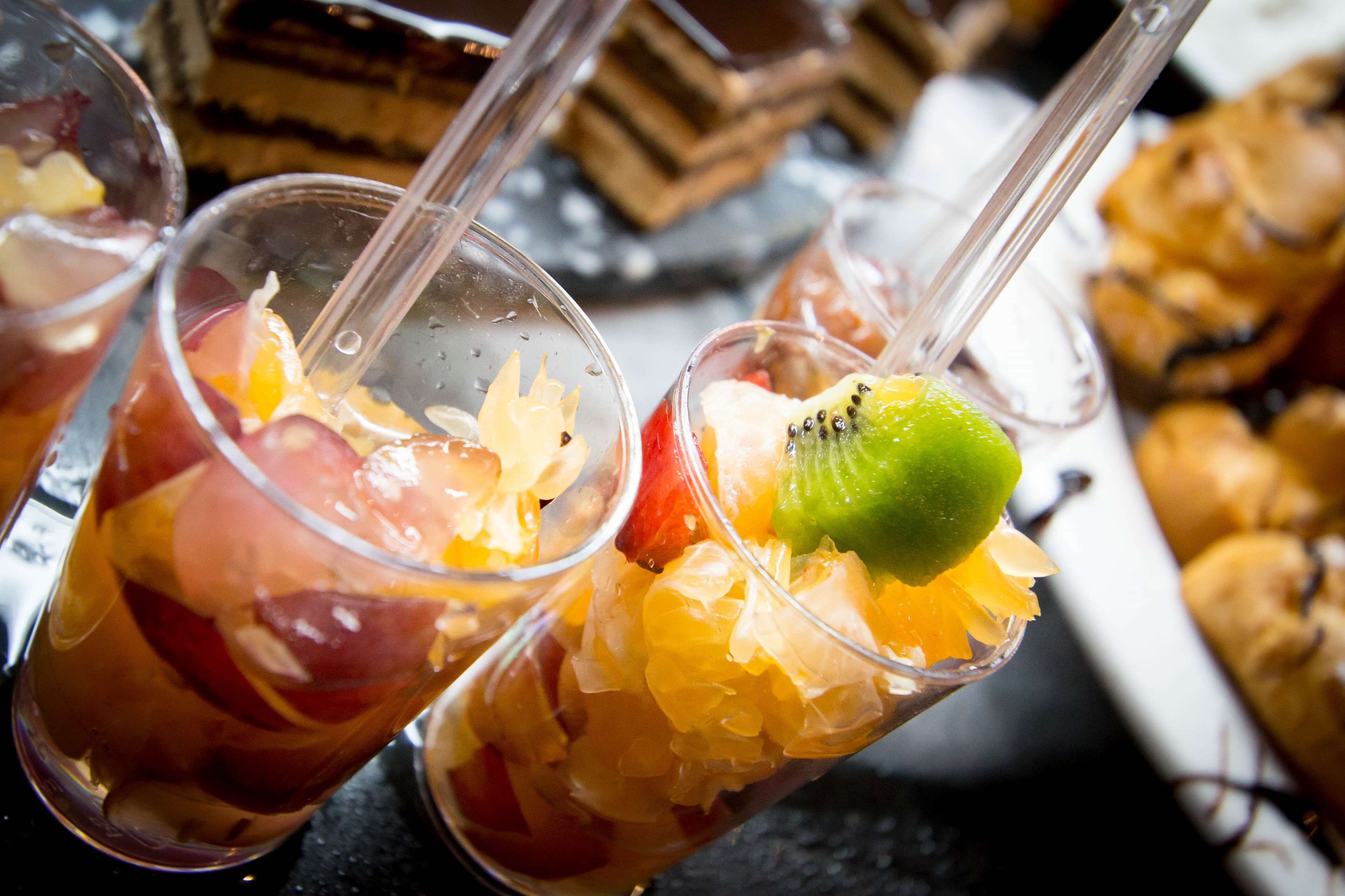 Tres vasos de ponche de frutas con pajitas, que contienen diversas frutas y cubitos de hielo.