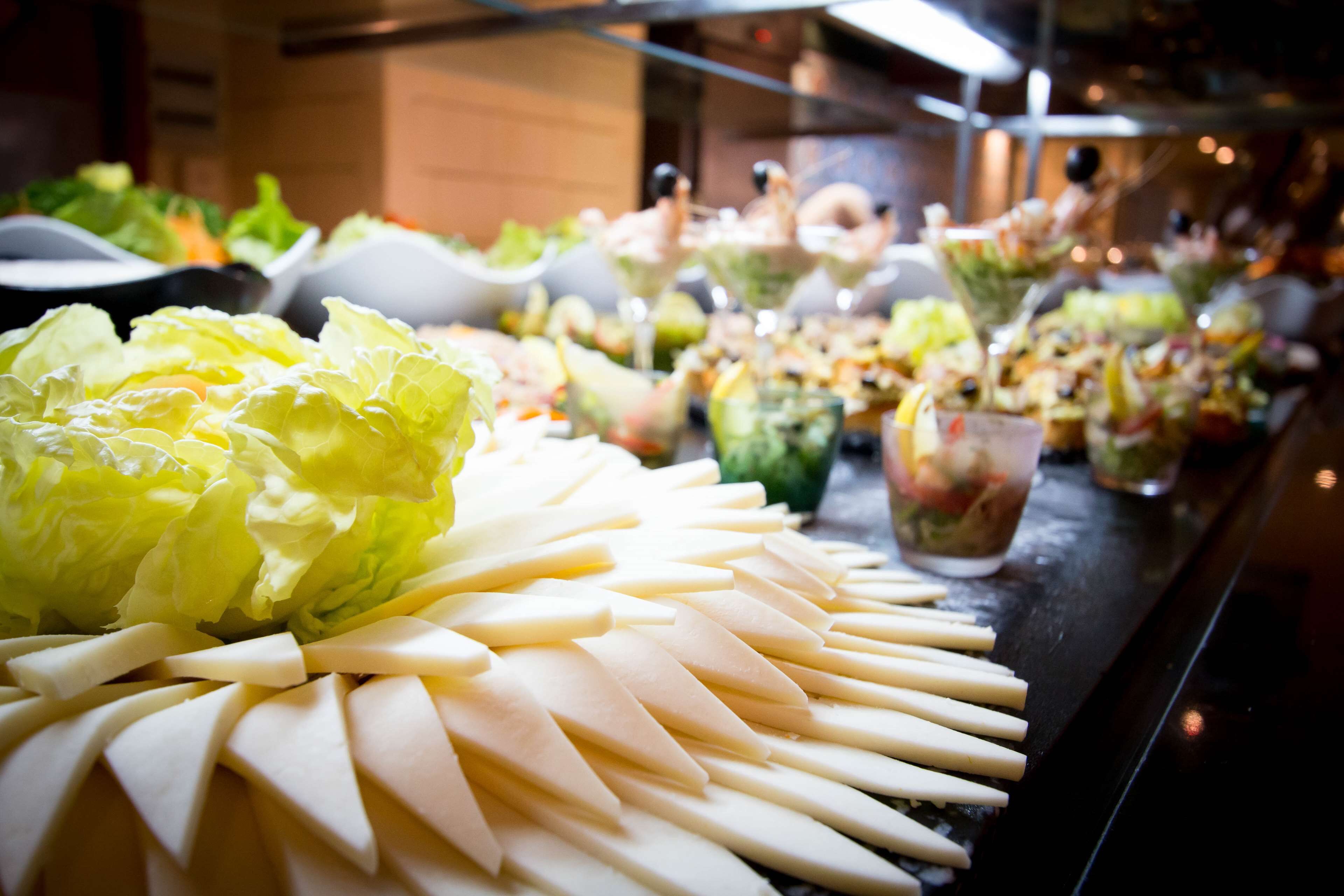 A buffet table with various food items including sliced cheese, salads, and a large head of lettuce.