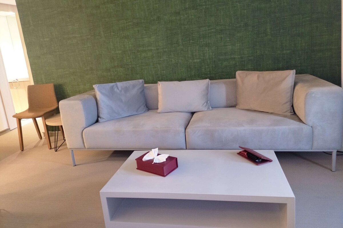 A modern living room with a light grey sofa, a small table, and a green textured wall.