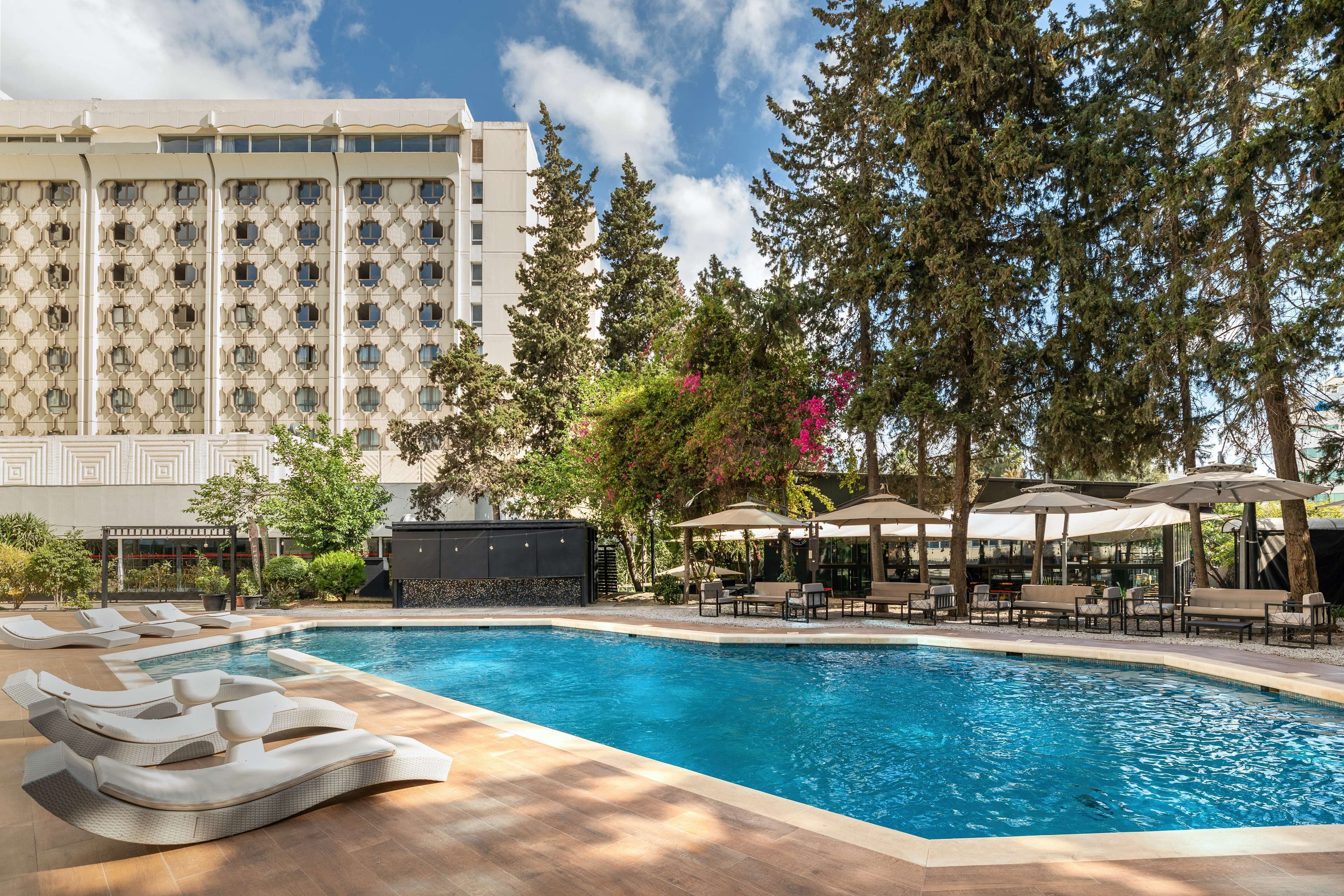 Una piscina con sillas de descanso, un jacuzzi y una zona de estar techada con sombrillas.