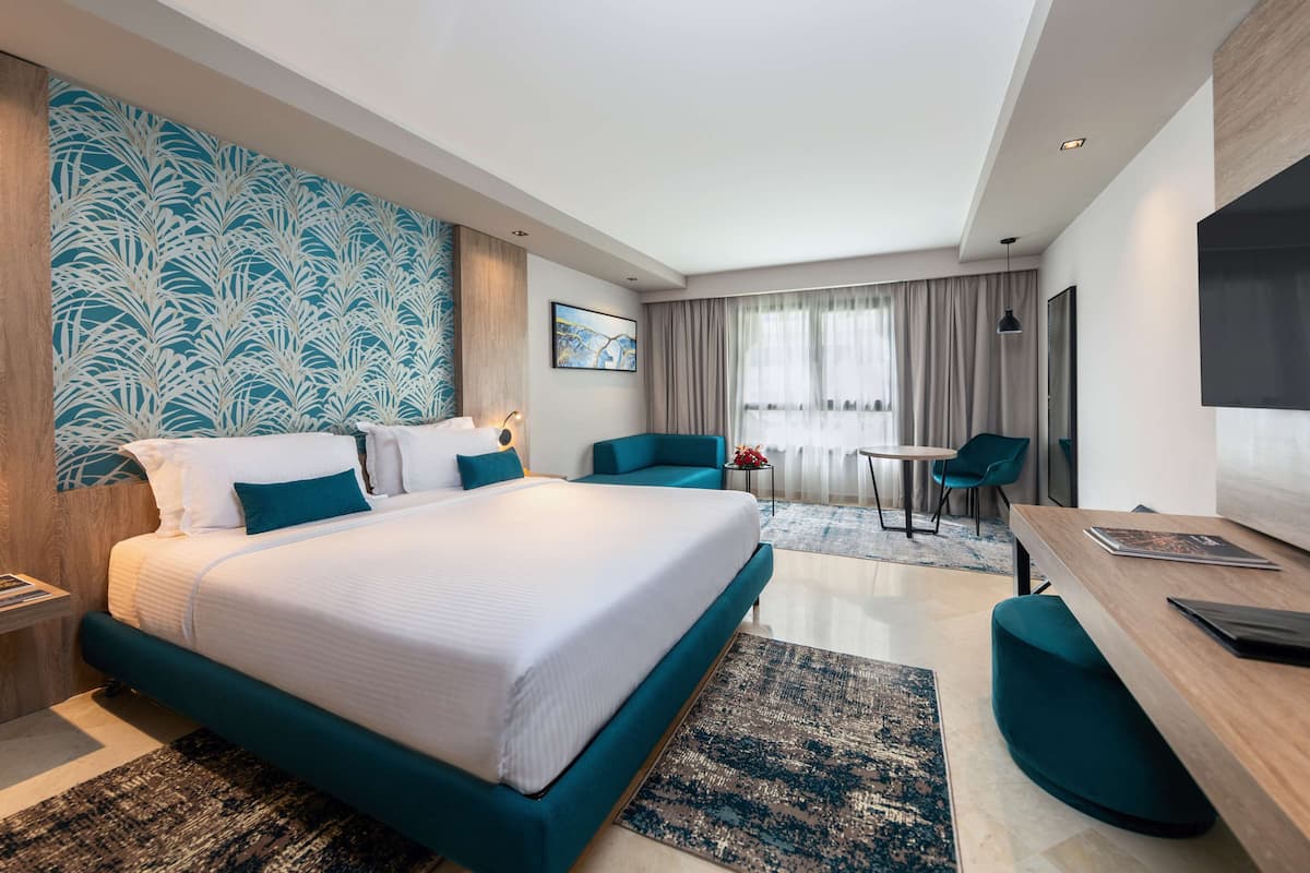 A modern hotel room with a large bed, a desk, a chair, and a TV.