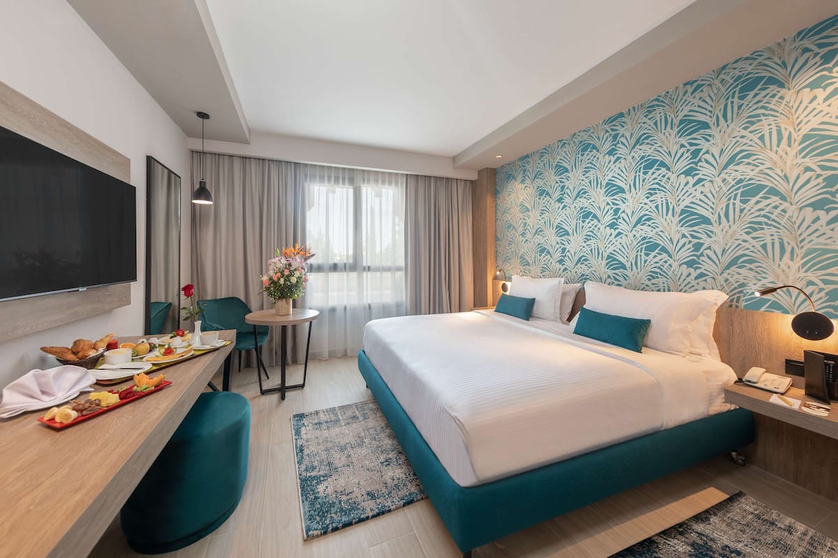 A hotel room with a bed, a desk with breakfast, a TV, and a window with curtains.
