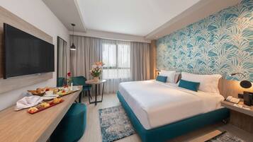 A hotel room with a bed, a desk with breakfast, a TV, and a window with curtains.