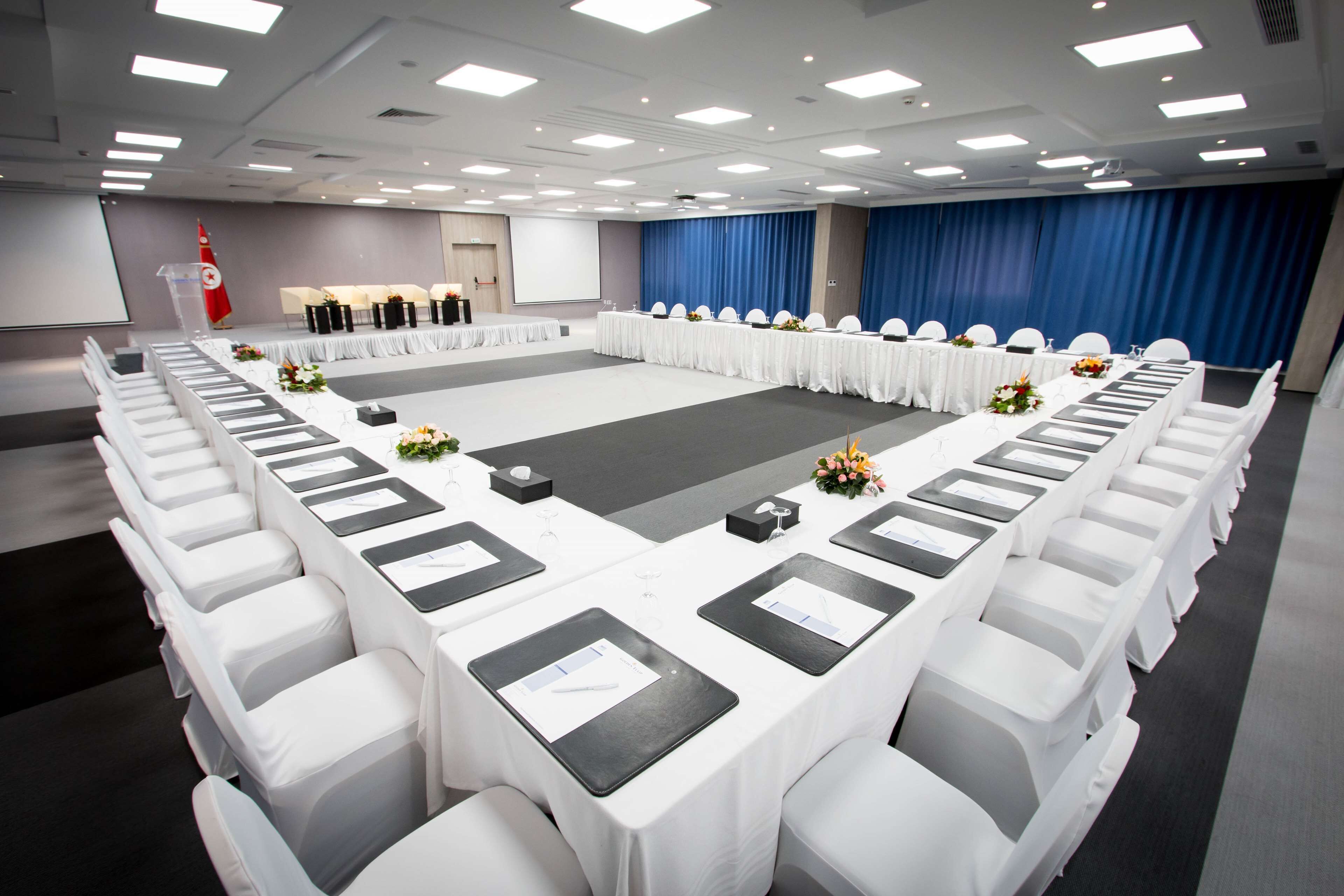 A conference room with a long table, white chairs, and a stage with a podium.