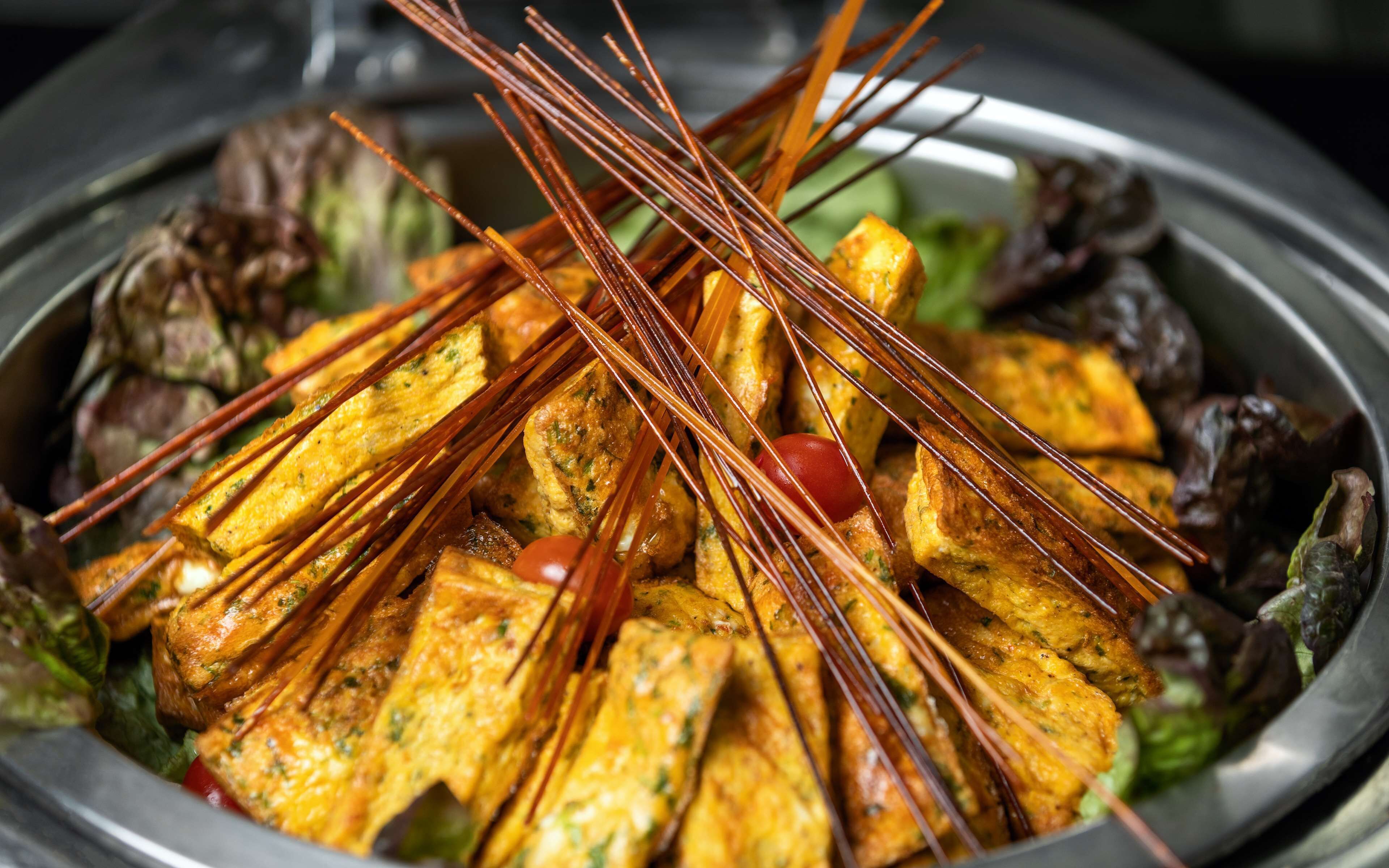 A dish with skewered food items, possibly a type of grilled or fried dish, served on a plate with some greens and vegetables.