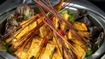 A dish with skewered food items, possibly a type of grilled or fried dish, served on a plate with some greens and vegetables.