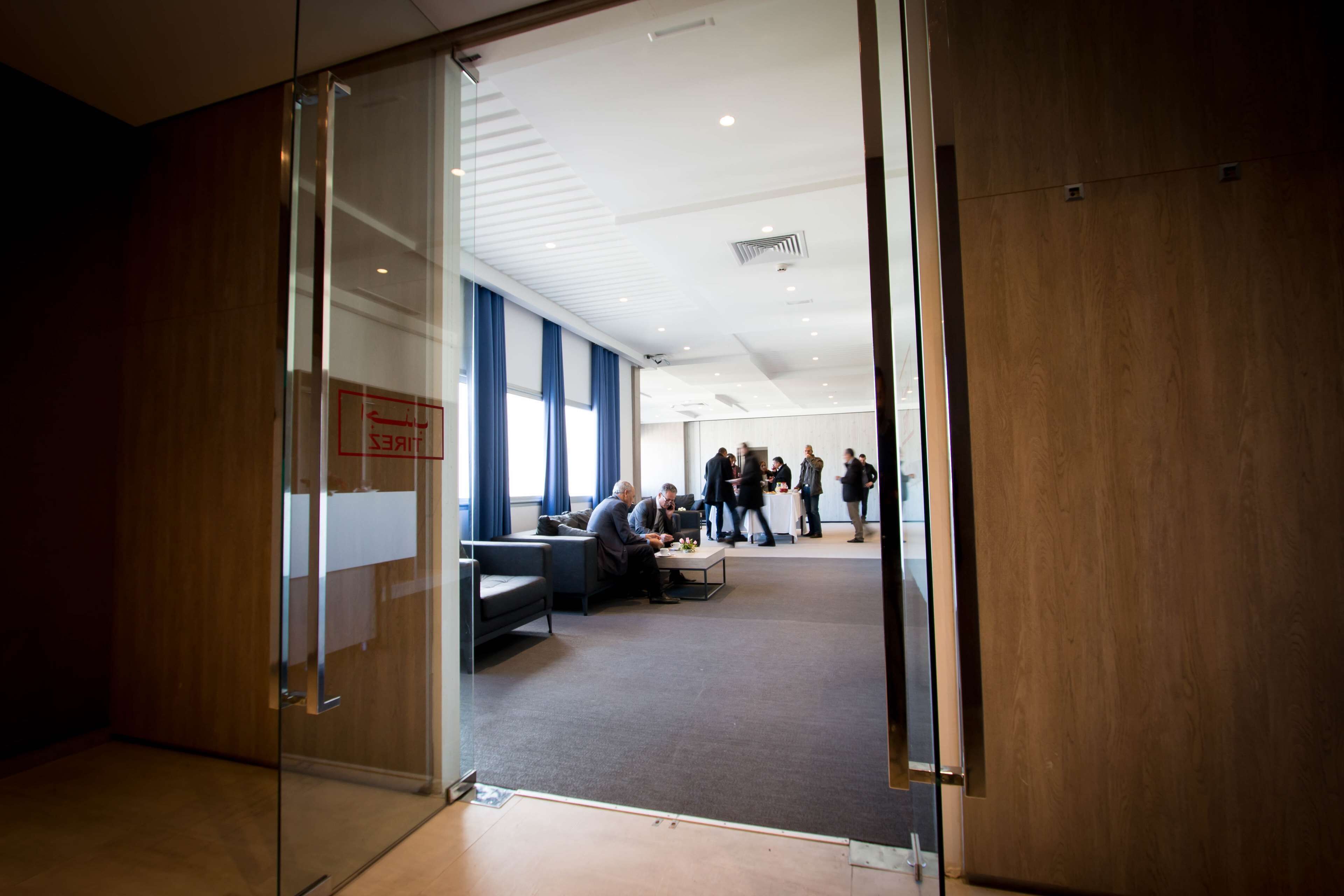Un espace de bureau moderne avec des portes en verre, un coin salon et un groupe de personnes à l’arrière-plan.