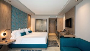 Una habitación de hotel moderna con una cama grande, un escritorio con una computadora portátil, un televisor y un rincón de descanso.