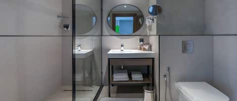 Un baño moderno con cabina de ducha de vidrio, un lavamanos con espejo, inodoro y un estante pequeño con toallas.