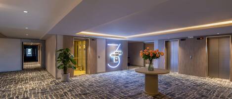 A hotel lobby with a patterned floor, a reception desk with a vase of flowers, and a digital sign indicating the 3rd floor.