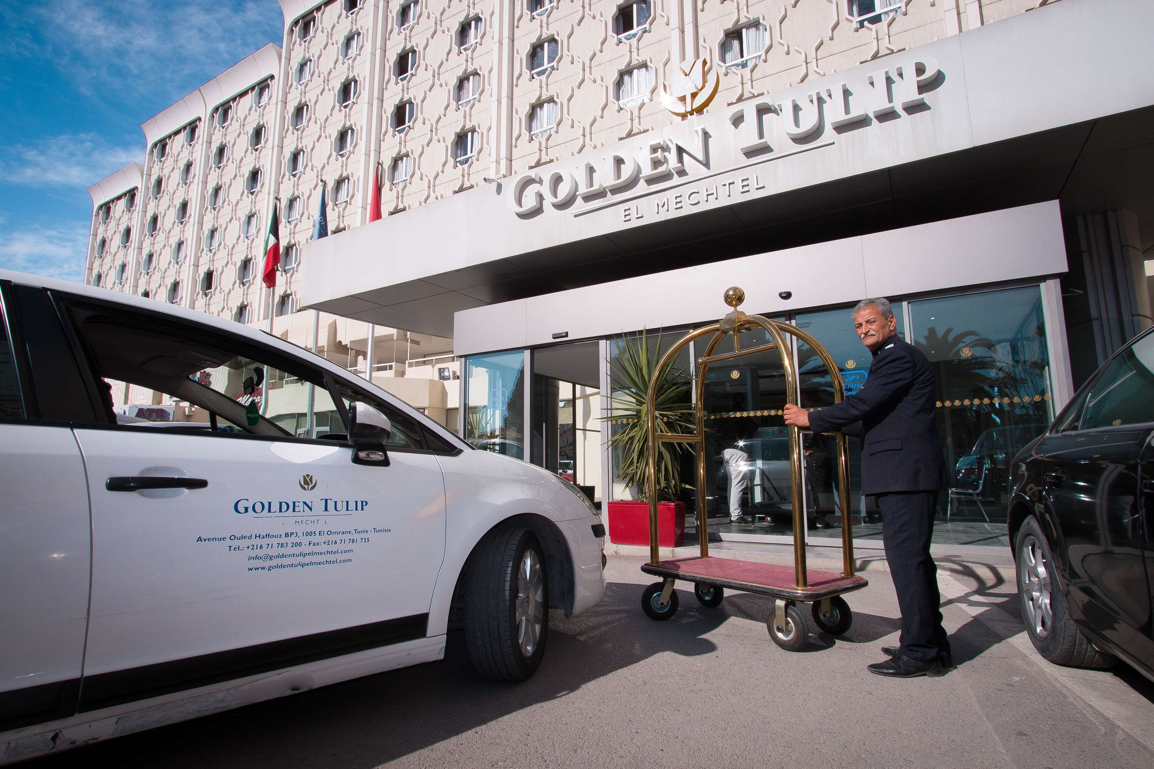 A white car with "Golden Tulip" branding parked in front of a building with a similar name.