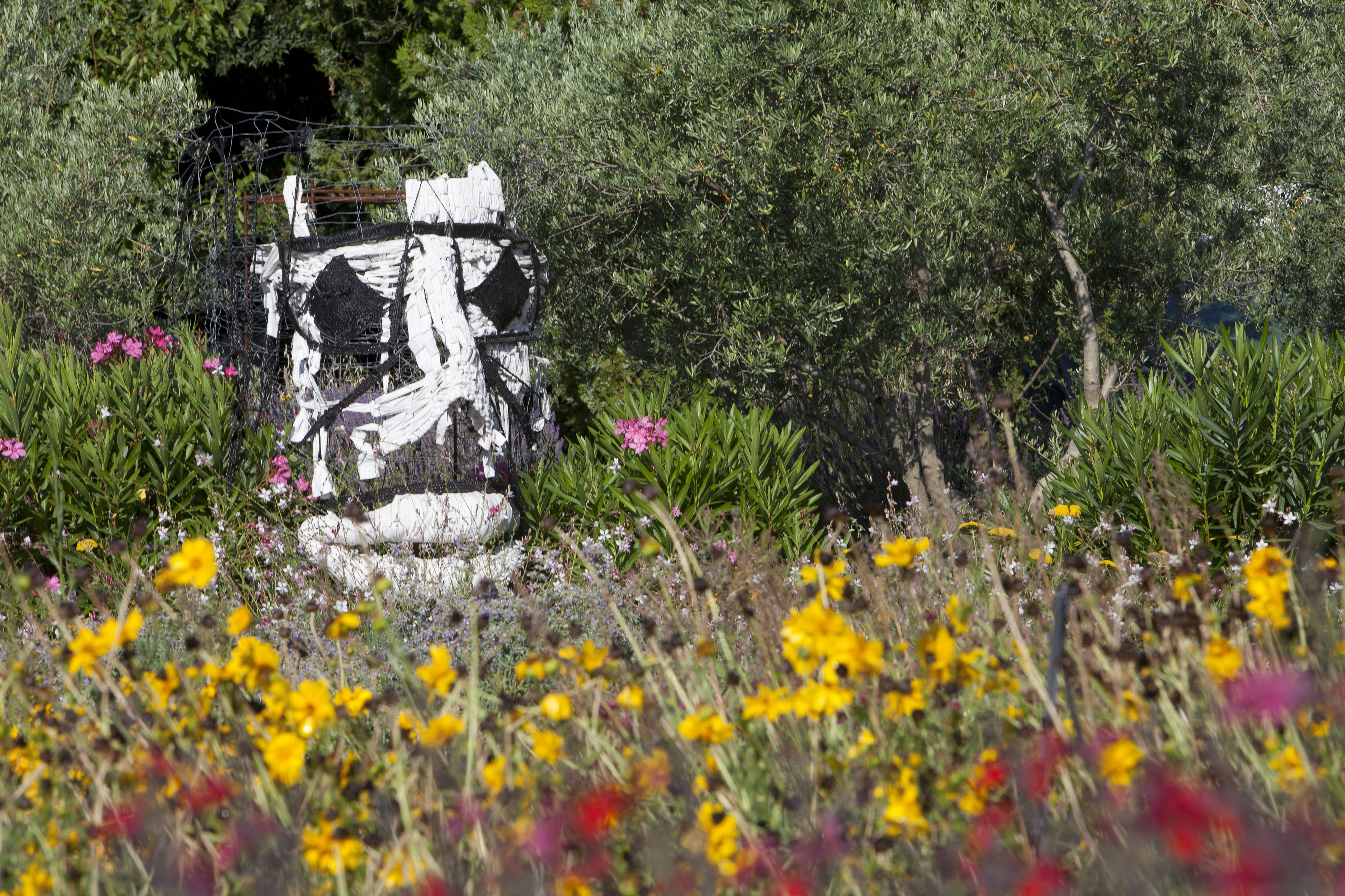 Un jardín con una escultura blanca rodeada de diversas flores y follaje.