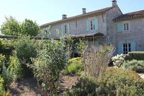 A stone building with light blue shutters and a garden in front.