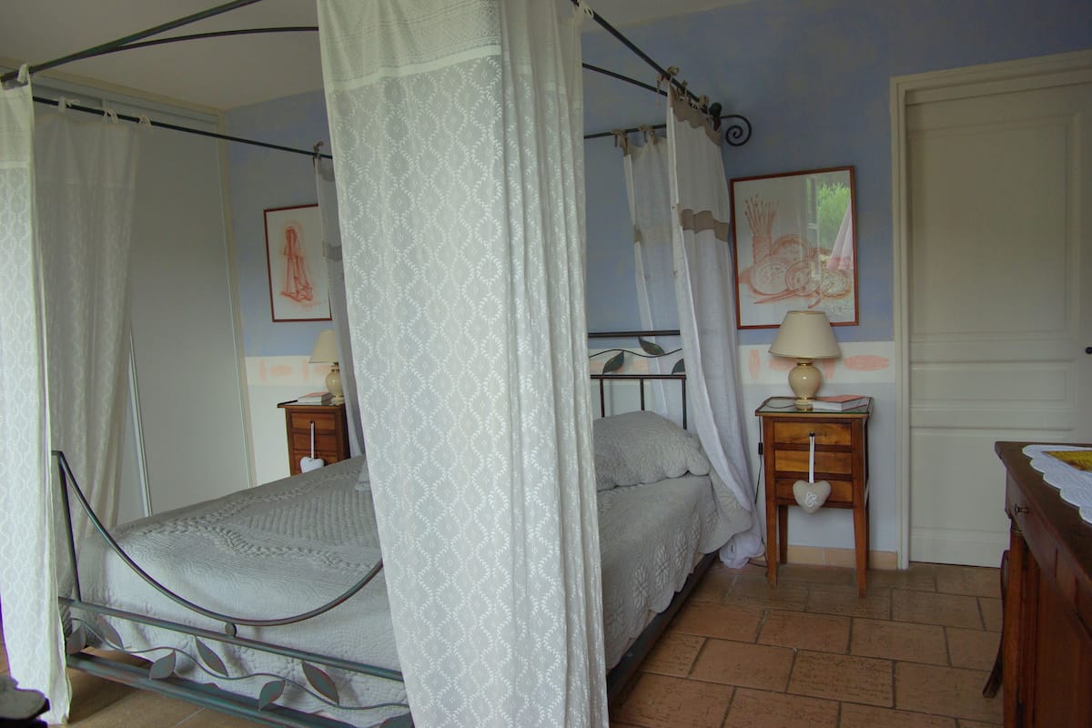 Ein Himmelbett mit Baldachin, ein Nachttisch mit Lampe und ein kleiner Nachttisch mit herzförmiger Dekoration.