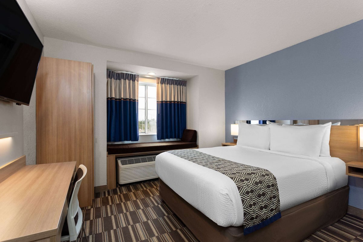 Habitación de hotel con cama, escritorio, televisión, ventana con cortinas y calefacción.